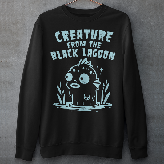 Make a splash with this fun twist on a horror classic! This sweatshirt features a playful cartoon version of the Gill-man, the iconic monster from Creature from the Black Lagoon. Above the illustration, bold retro lettering reads “CREATURE FROM THE BLACK LAGOON”, giving the design an authentic vintage movie-poster vibe. Perfect for monster movie fans, collectors of cult classics, or anyone who loves quirky, eye-catching style.