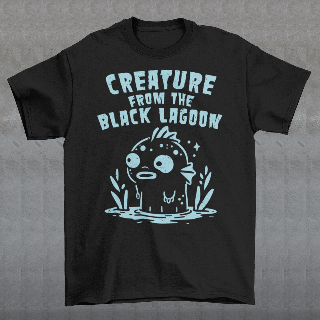 Make a splash with this fun twist on a horror classic! This t-shirt features a playful cartoon version of the Gill-man, the iconic monster from Creature from the Black Lagoon. Above the illustration, bold retro lettering reads “CREATURE FROM THE BLACK LAGOON”, giving the design an authentic vintage movie-poster vibe. Perfect for monster movie fans, collectors of cult classics, or anyone who loves quirky, eye-catching style.