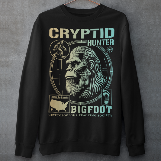 Illustration of a cryptozoology-themed sweatshirt featuring a stylized image of Bigfoot's head, shown with shaggy fur, deep-set eyes, and a mysterious expression. The artwork has a bold, rugged design in earthy tones, emphasizing the mythical nature of the creature. Above the image, the words "CRYPTID HUNTER" are prominently displayed in large, distressed lettering, suggesting adventure and mystery. The design appeals to fans of folklore, legends, and unexplained phenomena.