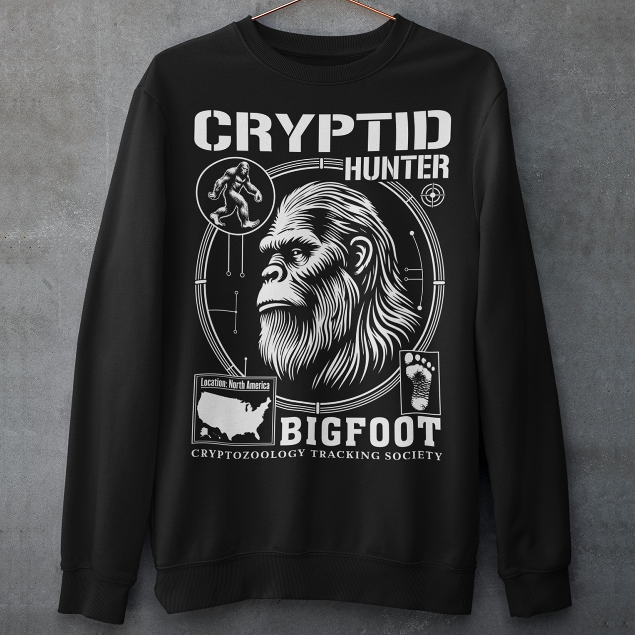 Illustration of a cryptozoology-themed sweatshirt featuring a stylized image of Bigfoot's head, shown with shaggy fur, deep-set eyes, and a mysterious expression. The artwork has a bold, rugged design in earthy tones, emphasizing the mythical nature of the creature. Above the image, the words "CRYPTID HUNTER" are prominently displayed in large, distressed lettering, suggesting adventure and mystery. The design appeals to fans of folklore, legends, and unexplained phenomena.
