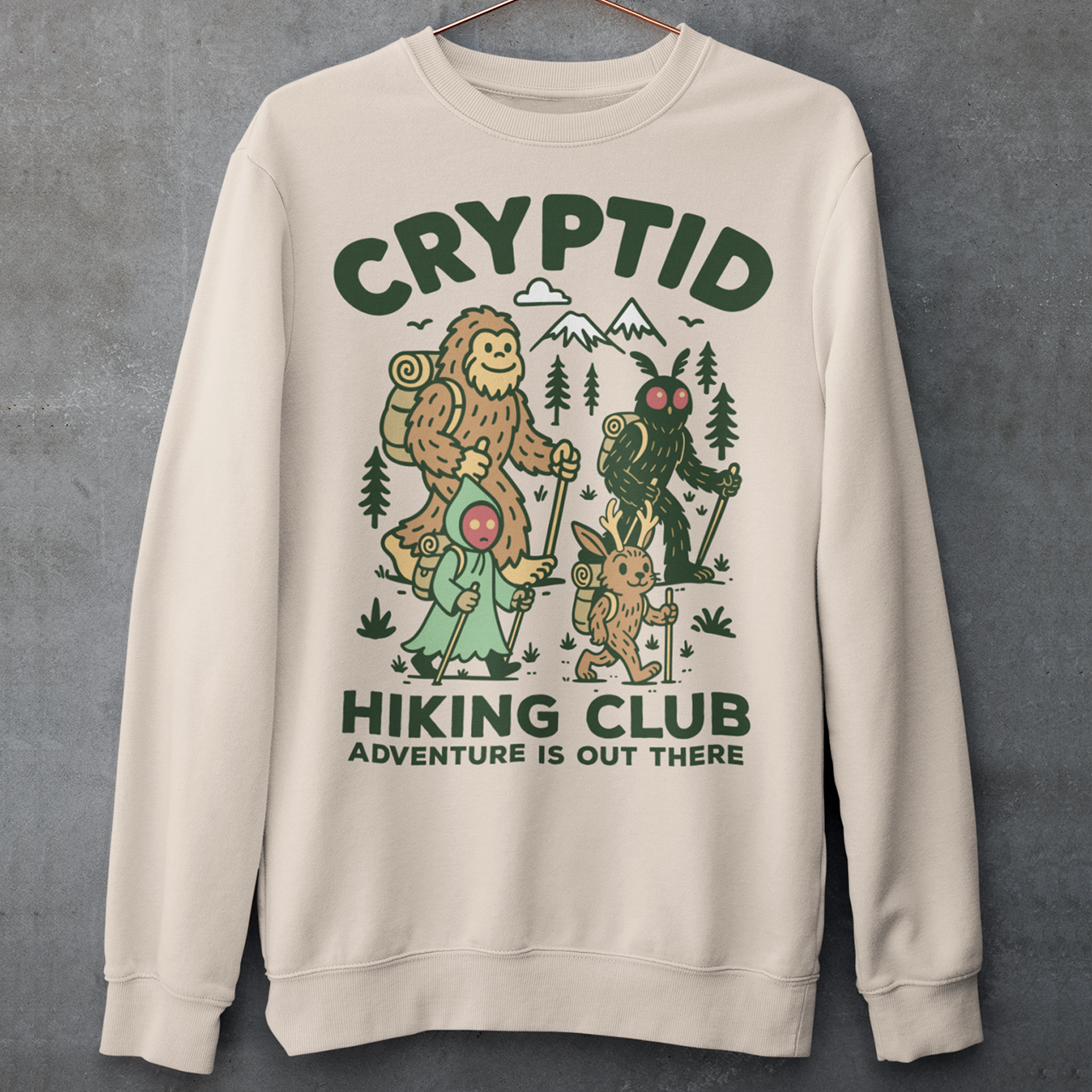 Beige sweatshirt featuring a playful “Cryptid Hiking Club” design with Bigfoot, Mothman, flatwoods monster, and a jackalope hiking together through a forest trail. The artwork includes mountains, pine trees, backpacks, and trekking poles with the slogan “Adventure Is Out There.” A fun outdoor-themed graphic perfect for cryptid fans, hikers, campers, paranormal enthusiasts, and lovers of folklore-inspired apparel.