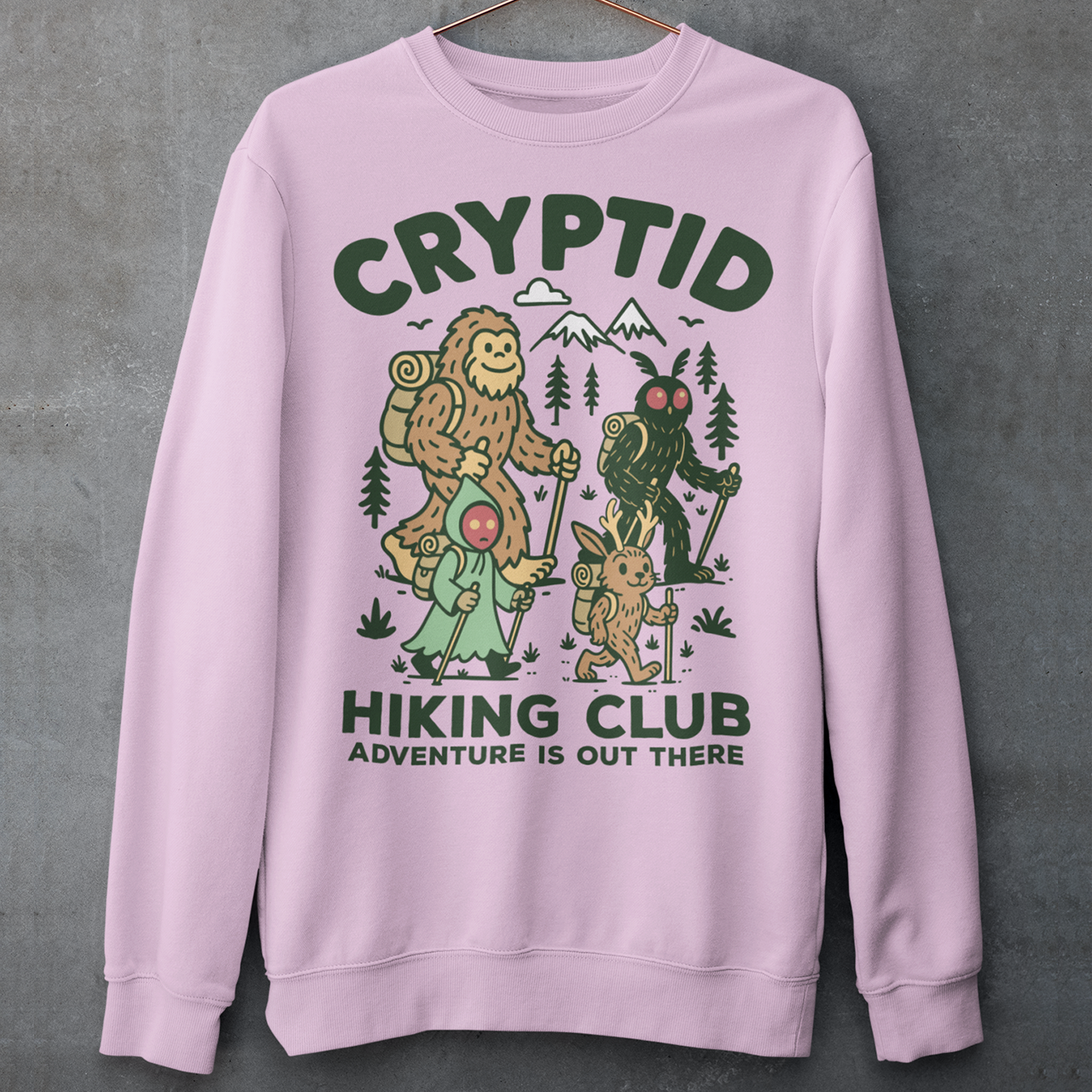 Pink sweatshirt featuring a playful “Cryptid Hiking Club” design with Bigfoot, Mothman, flatwoods monster, and a jackalope hiking together through a forest trail. The artwork includes mountains, pine trees, backpacks, and trekking poles with the slogan “Adventure Is Out There.” A fun outdoor-themed graphic perfect for cryptid fans, hikers, campers, paranormal enthusiasts, and lovers of folklore-inspired apparel.