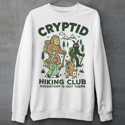 White sweatshirt featuring a playful “Cryptid Hiking Club” design with Bigfoot, Mothman, flatwoods monster, and a jackalope hiking together through a forest trail. The artwork includes mountains, pine trees, backpacks, and trekking poles with the slogan “Adventure Is Out There.” A fun outdoor-themed graphic perfect for cryptid fans, hikers, campers, paranormal enthusiasts, and lovers of folklore-inspired apparel.