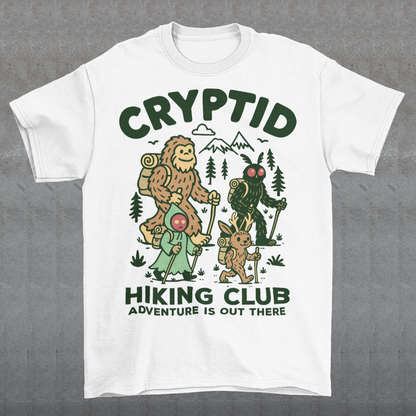 White t-shirt featuring a playful “Cryptid Hiking Club” design with Bigfoot, Mothman, flatwoods monster, and a jackalope hiking together through a forest trail. The artwork includes mountains, pine trees, backpacks, and trekking poles with the slogan “Adventure Is Out There.” A fun outdoor-themed graphic perfect for cryptid fans, hikers, campers, paranormal enthusiasts, and lovers of folklore-inspired apparel.