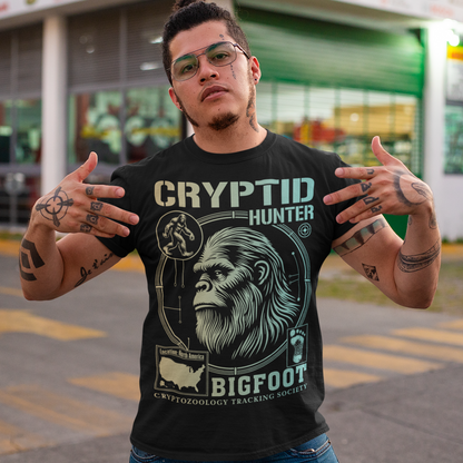 Illustration of a cryptozoology-themed t-shirt featuring a stylized image of Bigfoot's head, shown with shaggy fur, deep-set eyes, and a mysterious expression. The artwork has a bold, rugged design in earthy tones, emphasizing the mythical nature of the creature. Above the image, the words "CRYPTID HUNTER" are prominently displayed in large, distressed lettering, suggesting adventure and mystery. The design appeals to fans of folklore, legends, and unexplained phenomena.