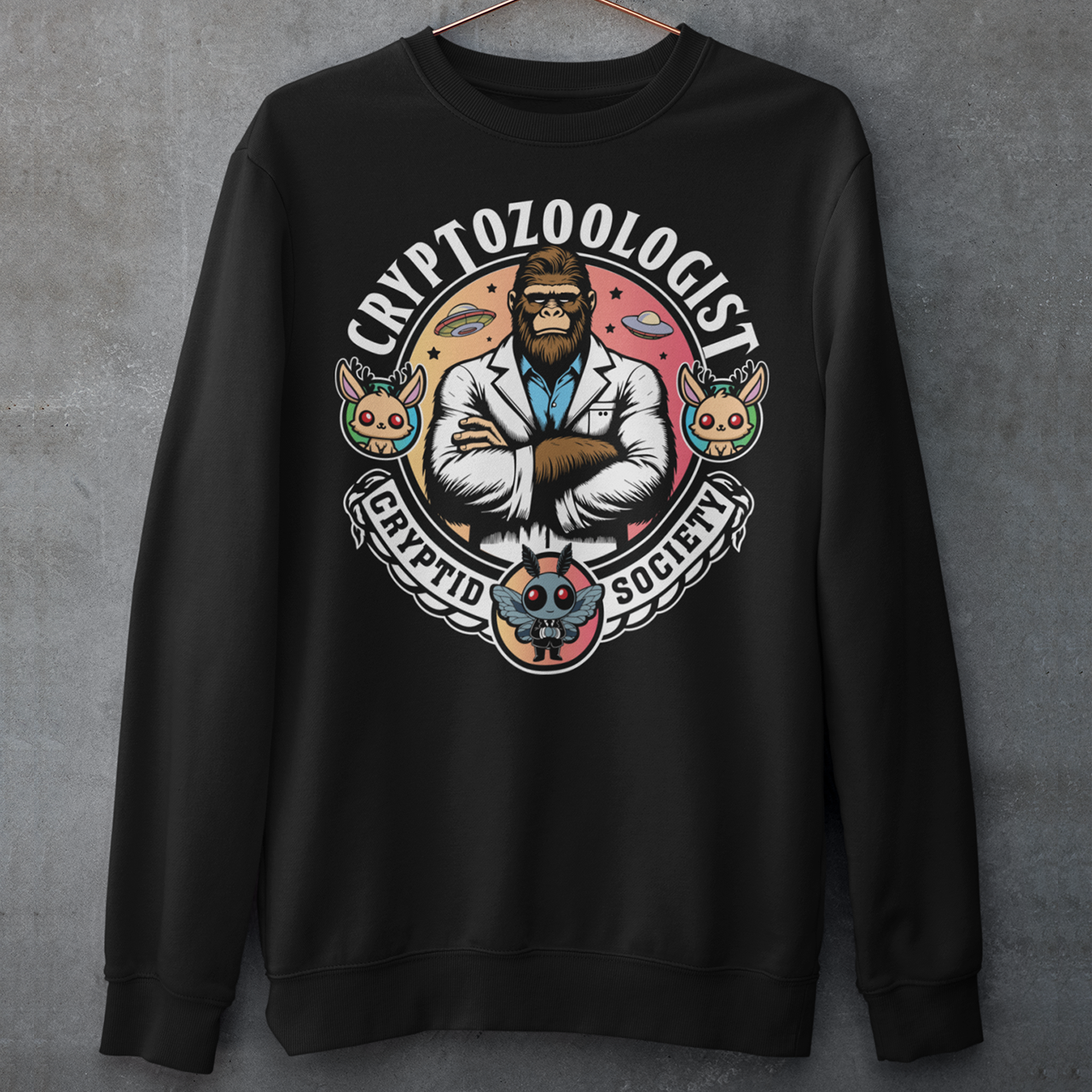 Black sweatshirt of a Bigfoot scientist with UFOs in the background. Mothman underneath and text above CRYPTOZOOLOGIST.