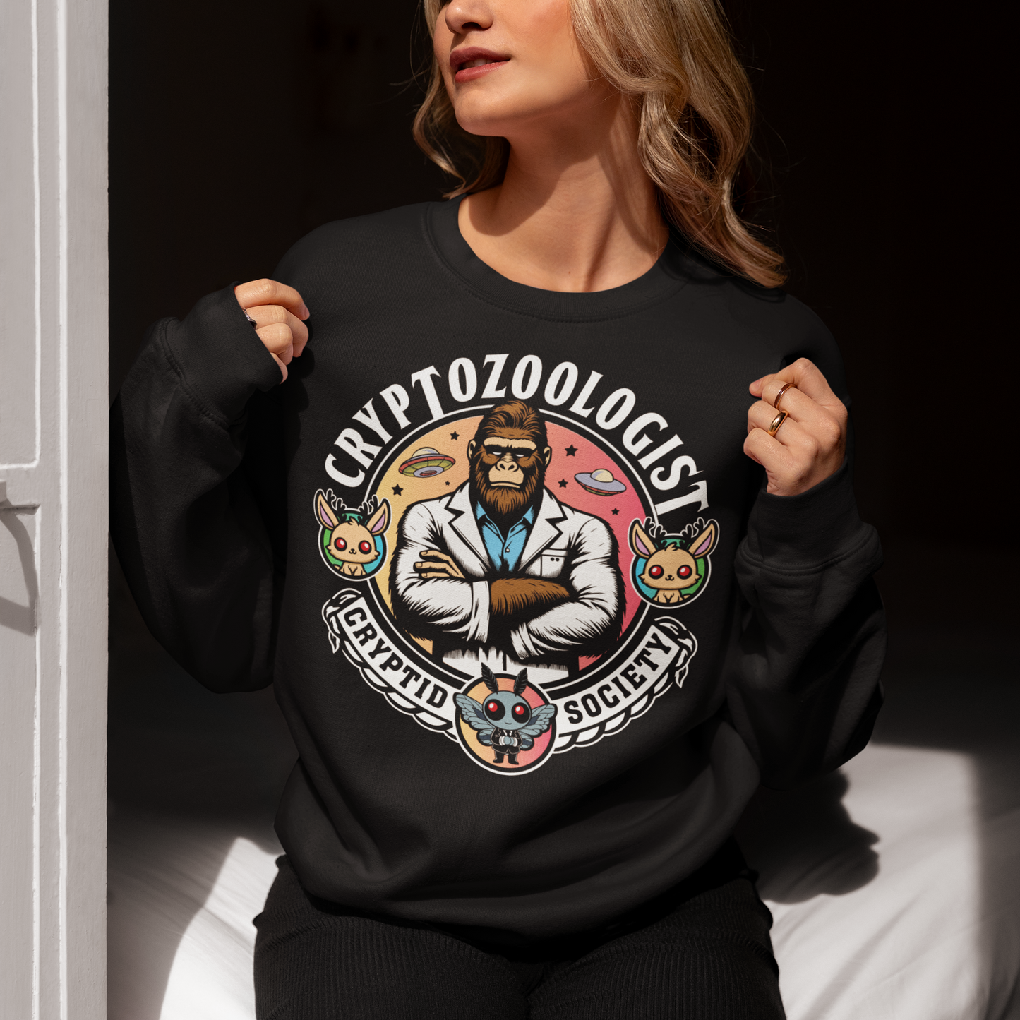 Black sweatshirt of a Bigfoot scientist with UFOs in the background. Mothman underneath and text above CRYPTOZOOLOGIST.