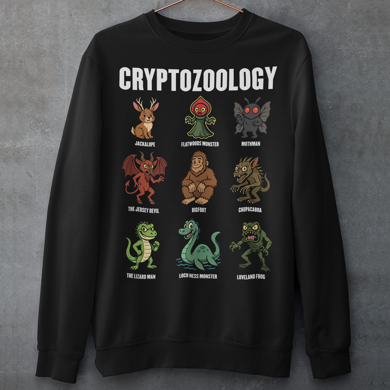 This black graphic sweatshirt celebrates the strange and wonderful world of cryptozoology with a lineup of iconic cryptids, each illustrated in a playful, cartoon style. From Bigfoot and Mothman to the Loch Ness Monster, Chupacabra, and Jersey Devil, the design reads like a greatest-hits roster of legendary creatures that lurk just beyond the edge of belief. Bold “Cryptozoology” lettering tops the grid, giving it the feel of a vintage science chart with a fun, modern twist.