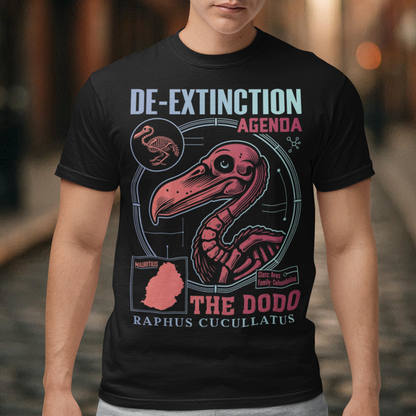 A graphic t-shirt featuring a stylized illustration of a dodo bird, standing upright with a proud, almost defiant expression. The dodo is depicted in vibrant colors, blending realism with a slightly cartoonish flair. Above the bird, bold, capitalized text reads "DE-EXTINCTION AGENDA" in a futuristic font, suggesting a science fiction or activist tone. The design evokes themes of genetic engineering, conservation, and the revival of extinct species. The shirt is a statement piece with humor.