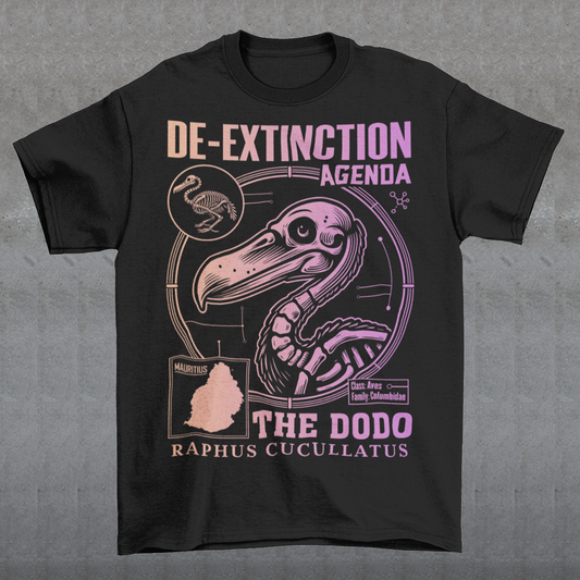 A graphic t-shirt featuring a stylized illustration of a dodo bird, standing upright with a proud, almost defiant expression. The dodo is depicted in vibrant colors, blending realism with a slightly cartoonish flair. Above the bird, bold, capitalized text reads "DE-EXTINCTION AGENDA" in a futuristic font, suggesting a science fiction or activist tone. The design evokes themes of genetic engineering, conservation, and the revival of extinct species. The shirt is a statement piece with humor.