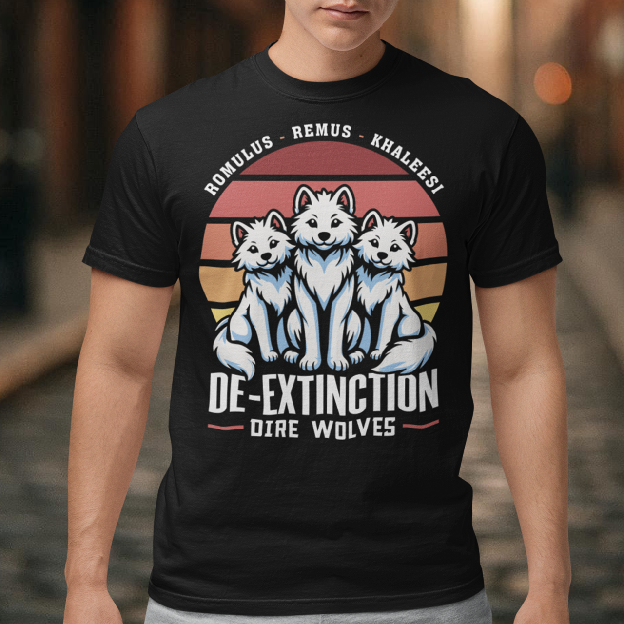 Unleash prehistoric power and style with this bold graphic tee featuring three majestic Dire Wolves sitting proudly in front of a vibrant retro sun. The wolves, detailed in a mix of shadow and light, capture the raw spirit of the Ice Age, while the backdrop—a nostalgic burst of sunset hues in retro stripes—adds a vintage sci-fi twist. Below the scene, the word DE-EXTINCTION is emblazoned in bold, futuristic typography, hinting at a world where ancient beasts rise again.