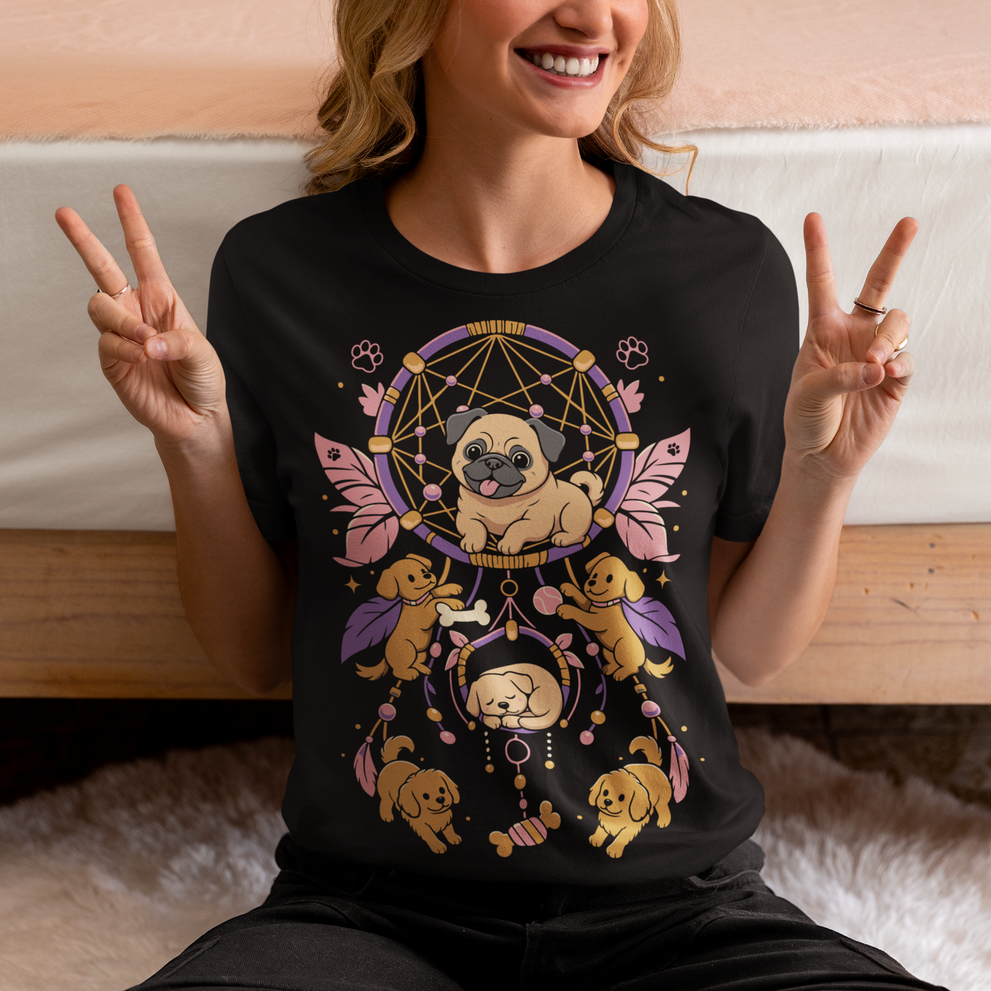 Black t-shirt featuring a colorful boho dog dream catcher design filled with adorable pug puppies. The artwork includes a central pug surrounded by smaller dogs, feathers, beads, paw prints, dog bones, and a sleeping puppy, creating a playful and whimsical pet-themed graphic. Perfect for pug lovers, dog moms, puppy enthusiasts, and fans of cute bohemian dog apparel.