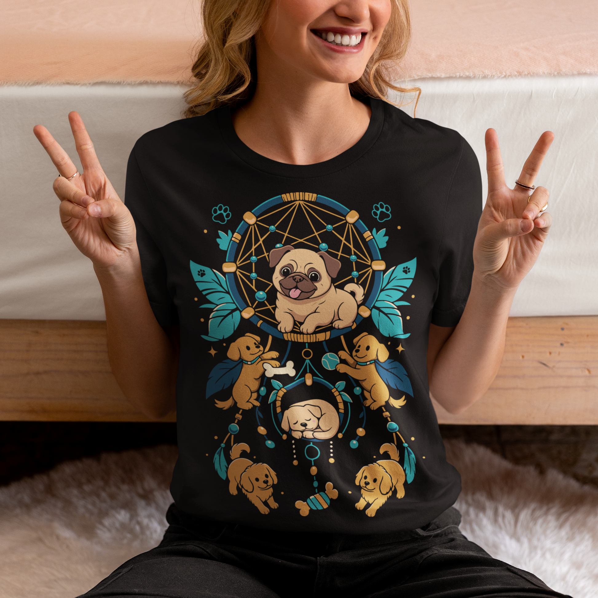 Black t-shirt featuring a colorful boho dog dream catcher design filled with adorable pug puppies. The artwork includes a central pug surrounded by smaller dogs, feathers, beads, paw prints, dog bones, and a sleeping puppy, creating a playful and whimsical pet-themed graphic. Perfect for pug lovers, dog moms, puppy enthusiasts, and fans of cute bohemian dog apparel.