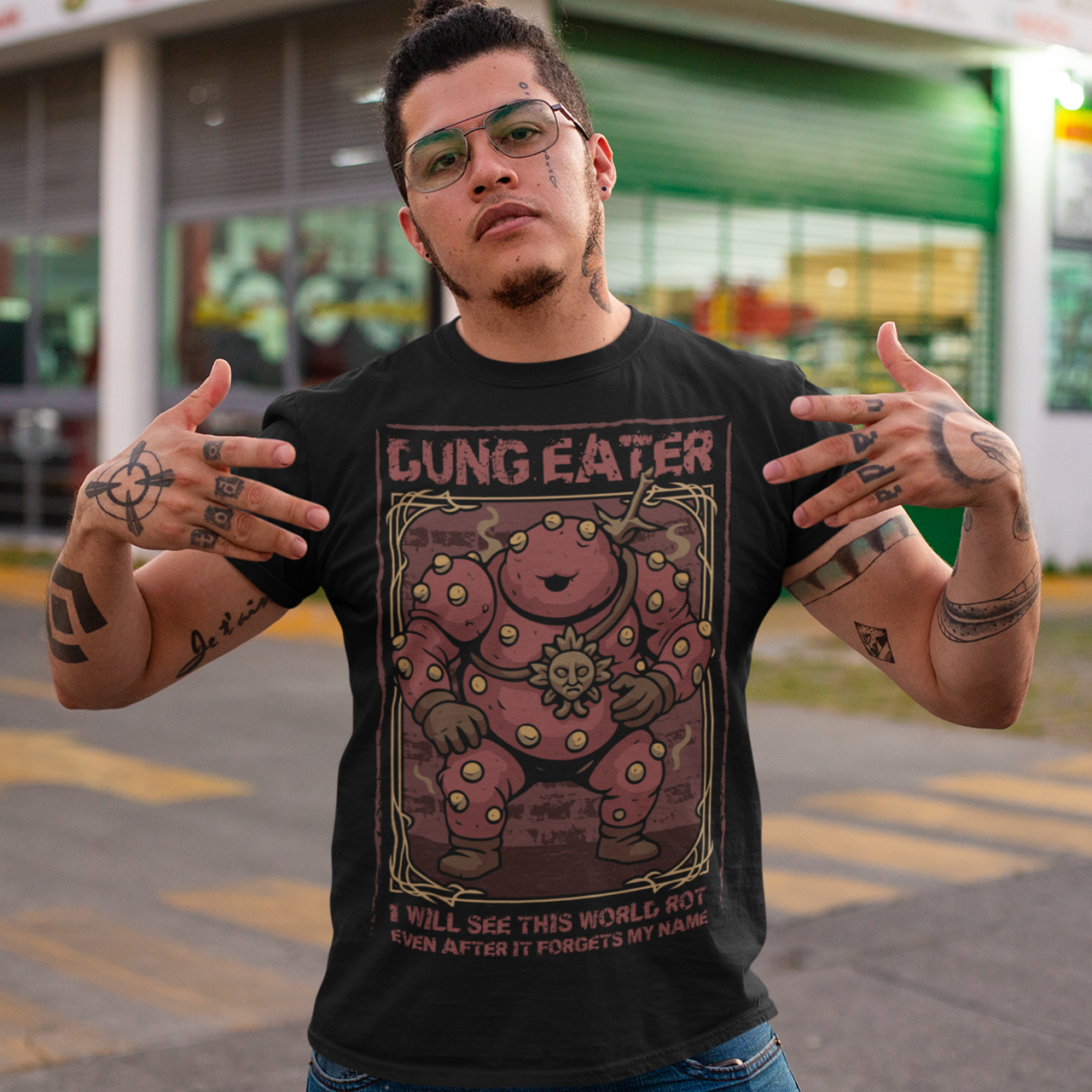 This black t-shirt features a grim, illustrated tribute to one of dark fantasy’s most unsettling figures Dung Eater. The hulking, corrupted character dominates the design, rendered in deep crimson tones with weathered textures and ornate framing that echo cursed tomes and forgotten prophecies. The bold title above and the chilling line below give the artwork the feeling of a forbidden page torn from a doomed legend.