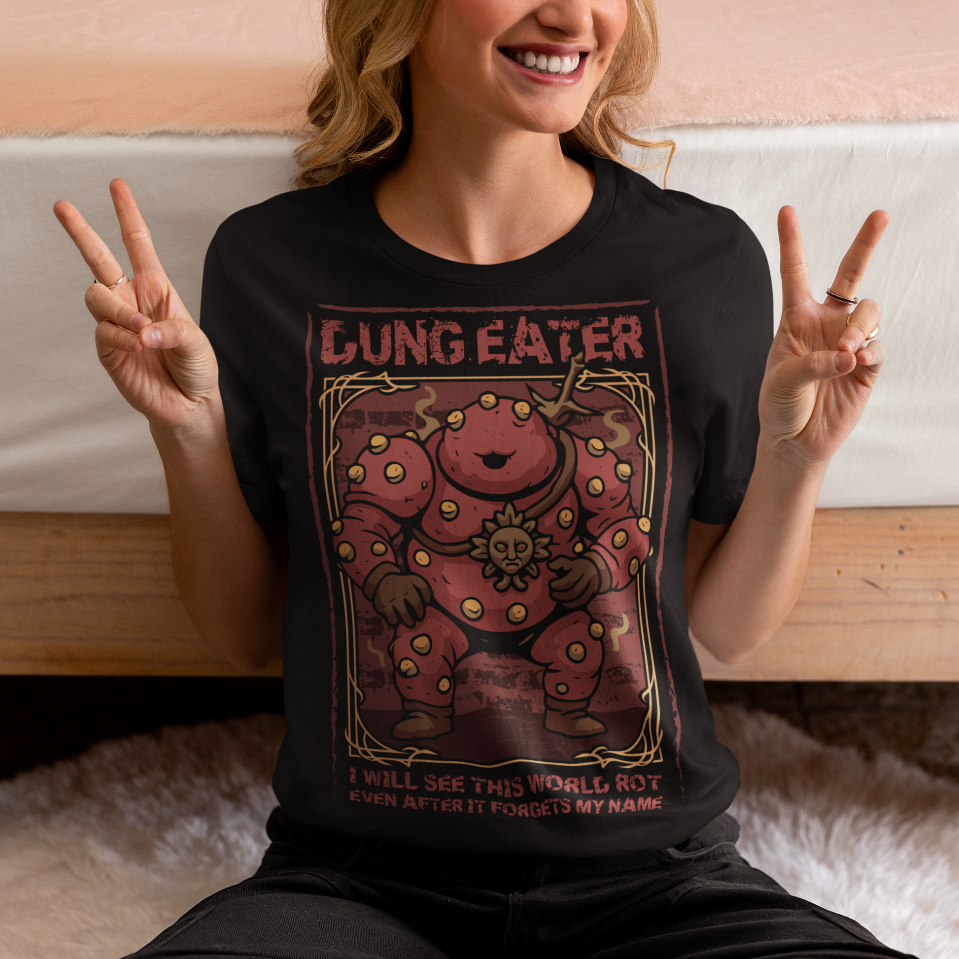 This black t-shirt features a grim, illustrated tribute to one of dark fantasy’s most unsettling figures Dung Eater. The hulking, corrupted character dominates the design, rendered in deep crimson tones with weathered textures and ornate framing that echo cursed tomes and forgotten prophecies. The bold title above and the chilling line below give the artwork the feeling of a forbidden page torn from a doomed legend.