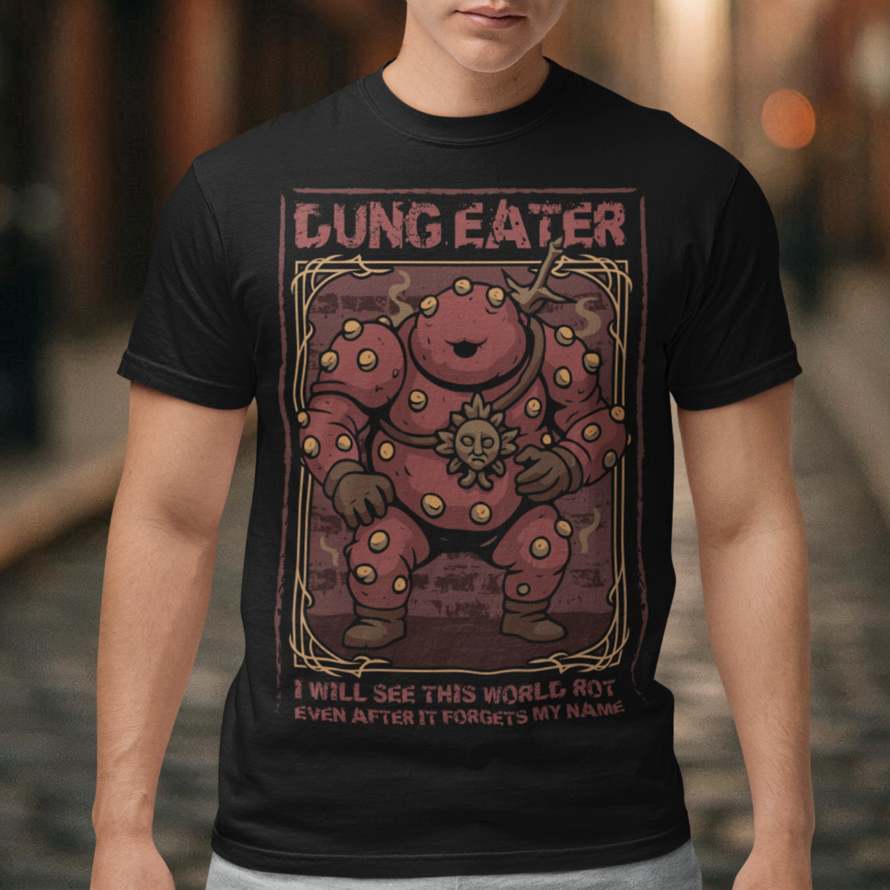 This black t-shirt features a grim, illustrated tribute to one of dark fantasy’s most unsettling figures Dung Eater. The hulking, corrupted character dominates the design, rendered in deep crimson tones with weathered textures and ornate framing that echo cursed tomes and forgotten prophecies. The bold title above and the chilling line below give the artwork the feeling of a forbidden page torn from a doomed legend.