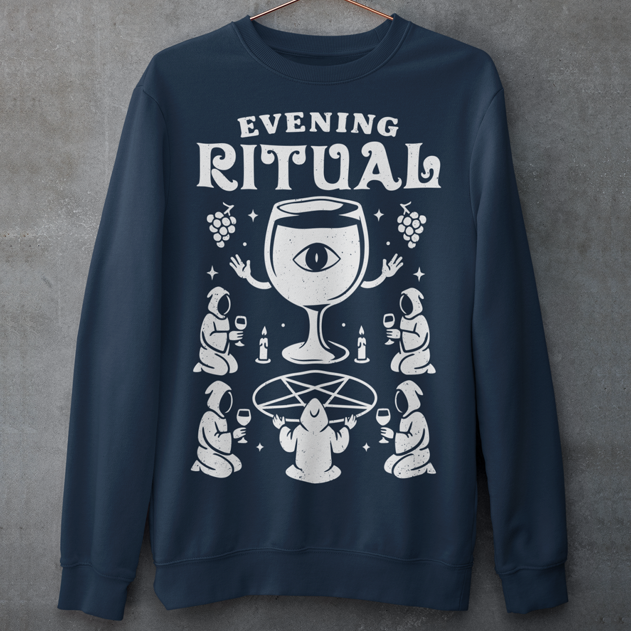 Navy sweatshirt featuring a white occult-style graphic with the text “Evening Ritual.” Design shows hooded figures gathered around a pentagram performing a ritual with wine glasses, candles, grapes, and a large mystical wine goblet with an eye symbol. Spooky gothic and illuminati-inspired humor combined with wine lover aesthetics.