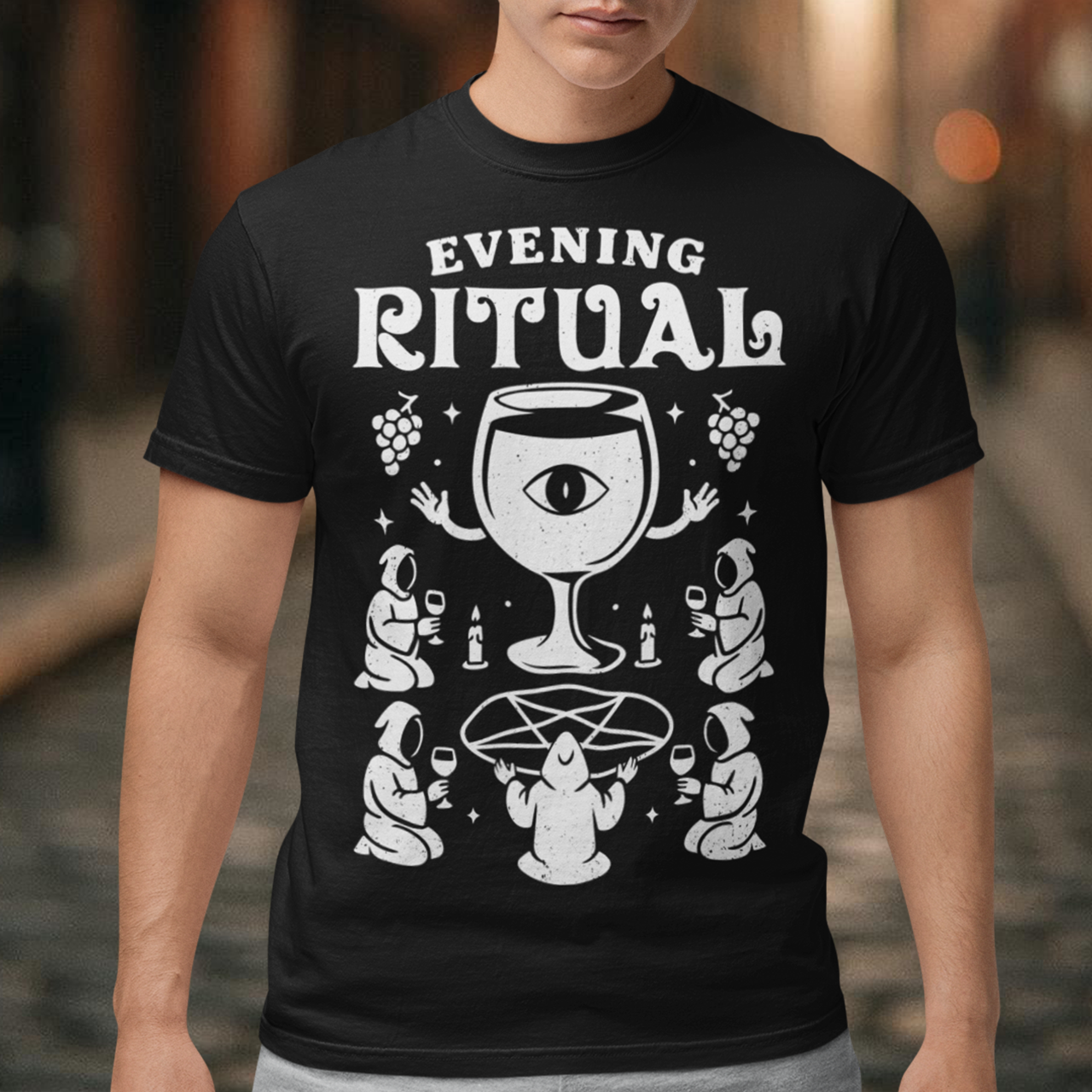 Black t-shirt featuring a white occult-style graphic with the text “Evening Ritual.” Design shows hooded figures gathered around a pentagram performing a ritual with wine glasses, candles, grapes, and a large mystical wine goblet with an eye symbol. Spooky gothic and illuminati-inspired humor combined with wine lover aesthetics.