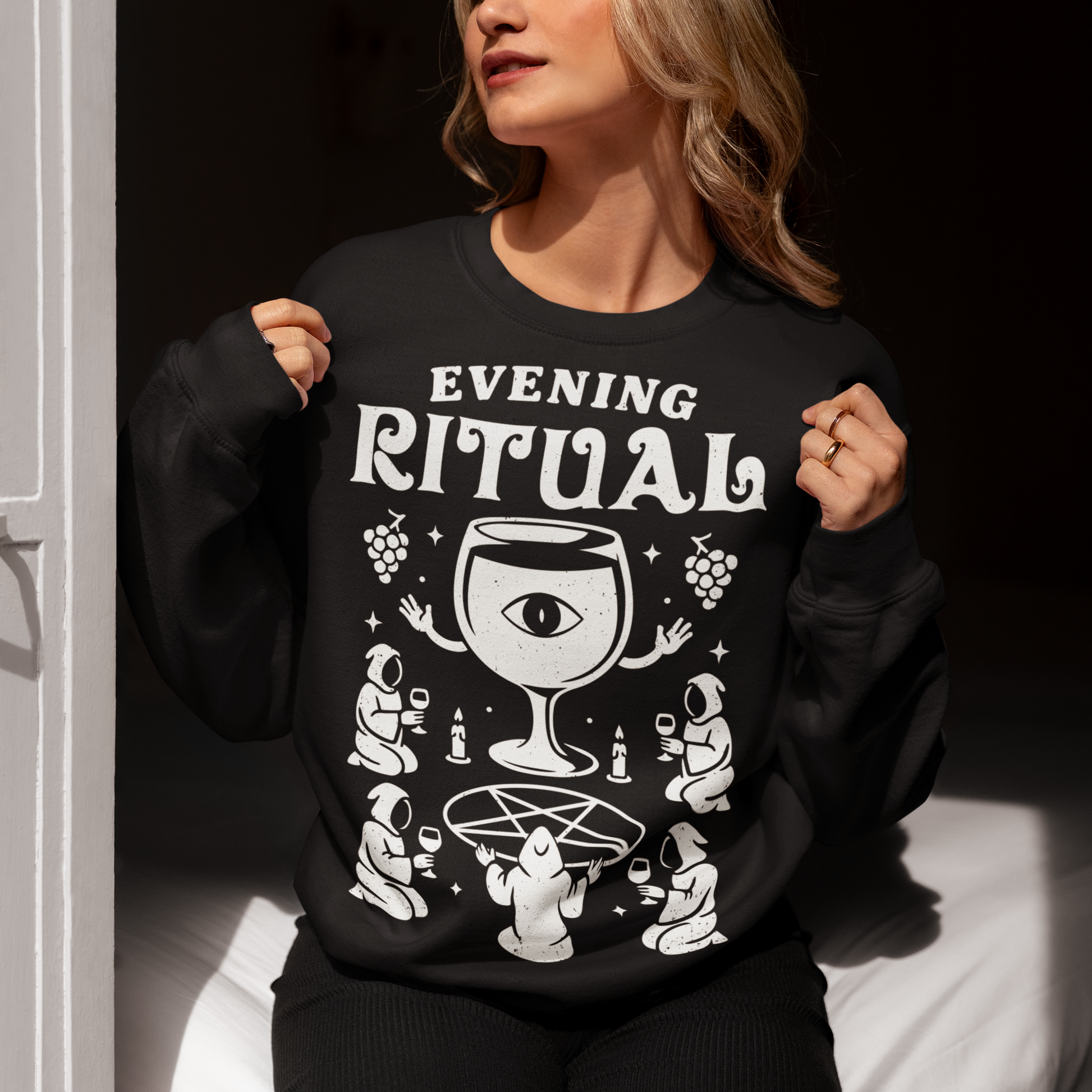 Black sweatshirt featuring a white occult-style graphic with the text “Evening Ritual.” Design shows hooded figures gathered around a pentagram performing a ritual with wine glasses, candles, grapes, and a large mystical wine goblet with an eye symbol. Spooky gothic and illuminati-inspired humor combined with wine lover aesthetics.