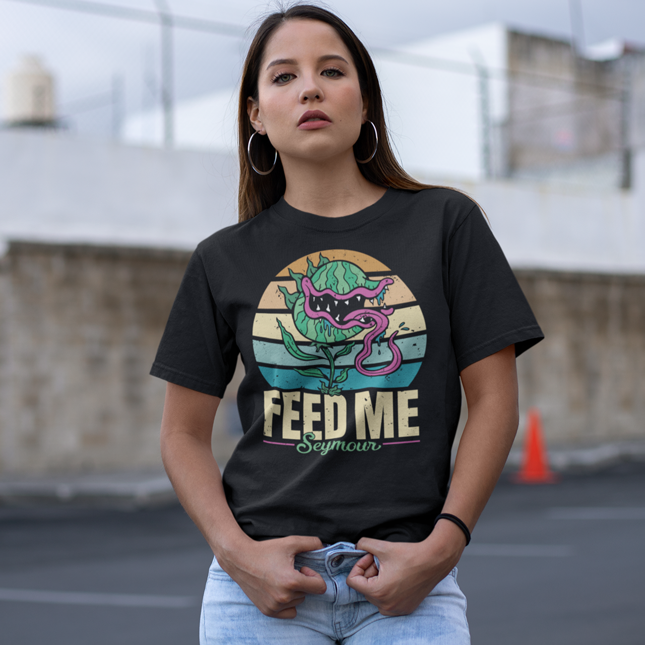 Black t-shirt of sentient carnivorous plant with a retro sun background with text underneath "FEED ME SEYMOUR".