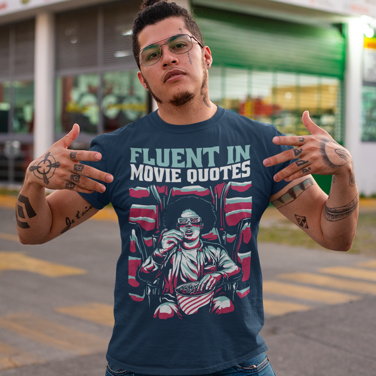 Navy t-shirt with a person wearing 3D glasses watching a movie in a cinema eating popcorn  with text "FLUENT IN MOVIE QUOTES".