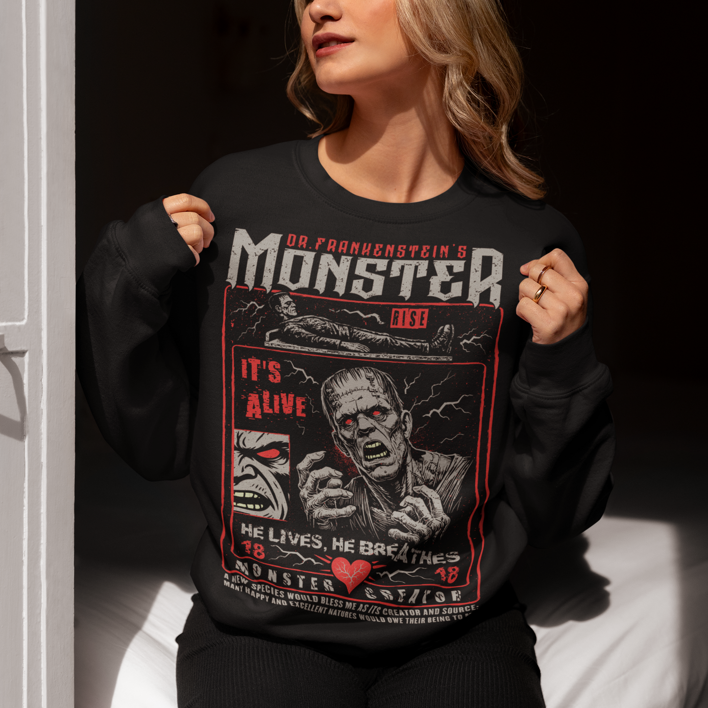 Black horror-themed sweatshirt featuring a vintage Frankenstein monster graphic in distressed gray print. The design includes comic-style panels with lightning bolts, Dr. Frankenstein’s monster rising from a lab table, and bold text reading “It’s Alive.” Gothic typography and retro horror artwork give the shirt a classic monster movie aesthetic, perfect for Halloween, horror fans, gothic fashion lovers, and collectors of vintage spooky apparel.