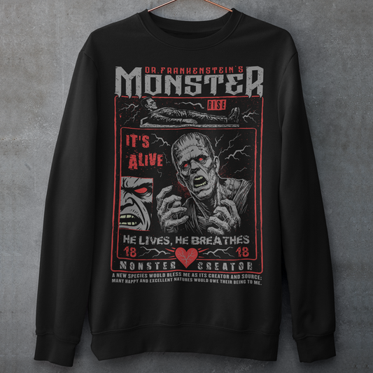 Black horror-themed sweatshirt featuring a vintage Frankenstein monster graphic in distressed gray print. The design includes comic-style panels with lightning bolts, Dr. Frankenstein’s monster rising from a lab table, and bold text reading “It’s Alive.” Gothic typography and retro horror artwork give the shirt a classic monster movie aesthetic, perfect for Halloween, horror fans, gothic fashion lovers, and collectors of vintage spooky apparel.