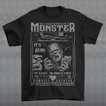 Black horror-themed t-shirt featuring a vintage Frankenstein monster graphic in distressed gray print. The design includes comic-style panels with lightning bolts, Dr. Frankenstein’s monster rising from a lab table, and bold text reading “It’s Alive.” Gothic typography and retro horror artwork give the shirt a classic monster movie aesthetic, perfect for Halloween, horror fans, gothic fashion lovers, and collectors of vintage spooky apparel.