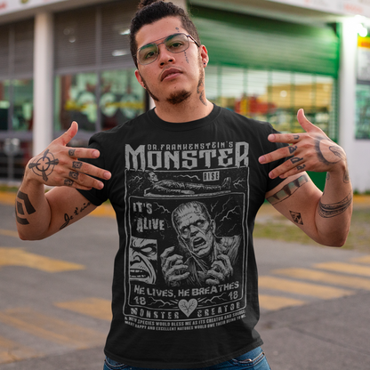 Black horror-themed t-shirt featuring a vintage Frankenstein monster graphic in distressed gray print. The design includes comic-style panels with lightning bolts, Dr. Frankenstein’s monster rising from a lab table, and bold text reading “It’s Alive.” Gothic typography and retro horror artwork give the shirt a classic monster movie aesthetic, perfect for Halloween, horror fans, gothic fashion lovers, and collectors of vintage spooky apparel.