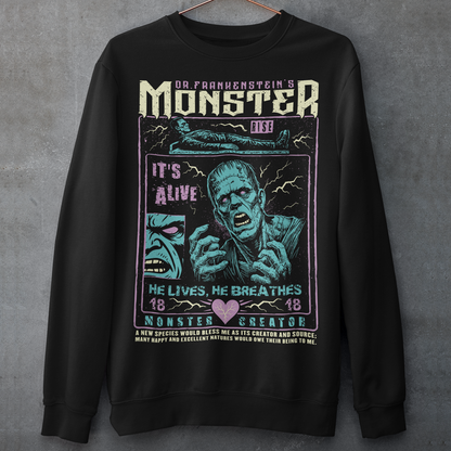 Black horror-themed sweatshirt featuring a vintage Frankenstein monster graphic in distressed gray print. The design includes comic-style panels with lightning bolts, Dr. Frankenstein’s monster rising from a lab table, and bold text reading “It’s Alive.” Gothic typography and retro horror artwork give the shirt a classic monster movie aesthetic, perfect for Halloween, horror fans, gothic fashion lovers, and collectors of vintage spooky apparel.