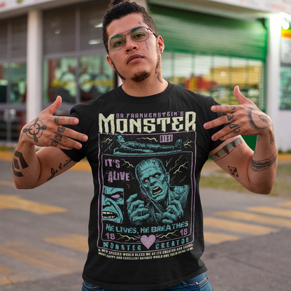 Black horror-themed t-shirt featuring a vintage Frankenstein monster graphic in distressed gray print. The design includes comic-style panels with lightning bolts, Dr. Frankenstein’s monster rising from a lab table, and bold text reading “It’s Alive.” Gothic typography and retro horror artwork give the shirt a classic monster movie aesthetic, perfect for Halloween, horror fans, gothic fashion lovers, and collectors of vintage spooky apparel.
