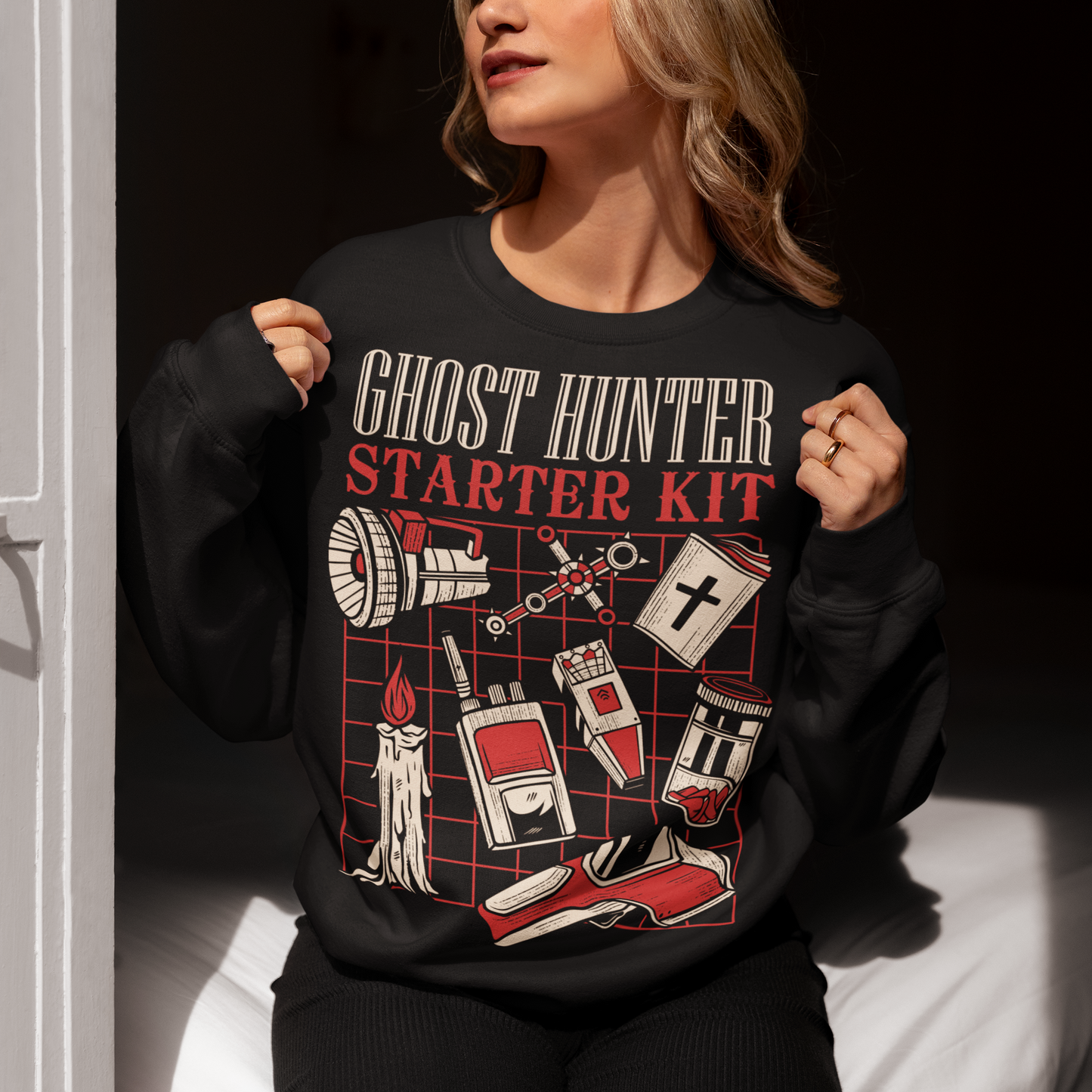 Step into the shadows with this Ghost Hunter Starter Kit sweatshirt, a perfect blend of spooky humor and paranormal adventure. Designed for fans of ghost hunting, horror culture, and all things supernatural, this bold graphic tee features a vintage-style layout packed with classic ghost hunting essentials like an EMF reader, flashlight, candle, spirit box, holy book, and more. The striking red and off-white artwork pops against the black fabric, giving it a retro paranormal investigator vibe.