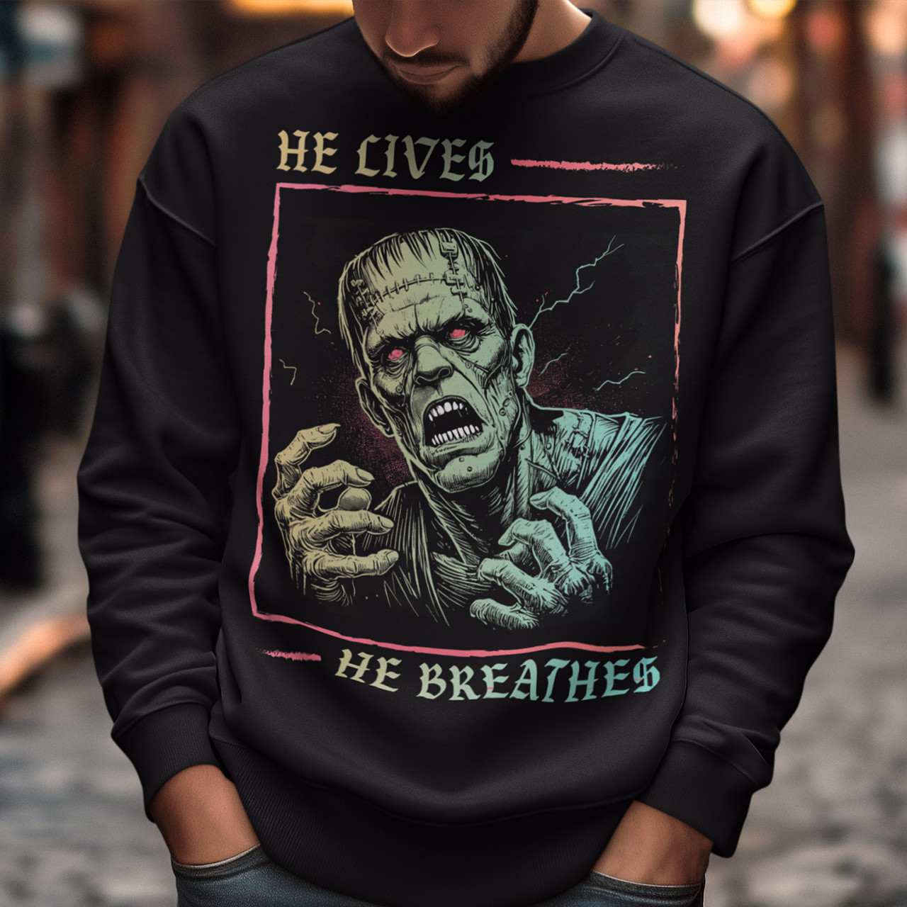 Black sweatshirt of Frankenstein with text above HE LIVES and text below HE BREATHES.
