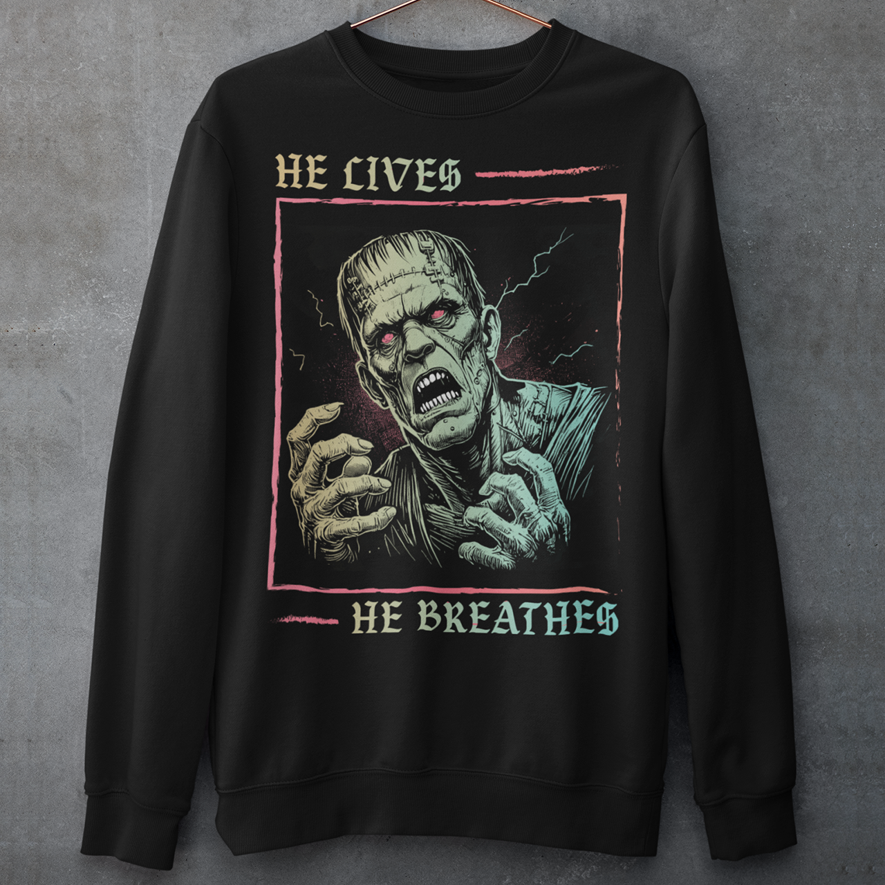 Black sweatshirt of Frankenstein with text above HE LIVES and text below HE BREATHES.