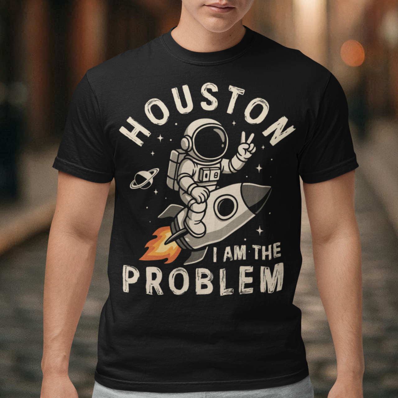 Make a statement that’s out of this world. This bold graphic tee features a fearless astronaut riding a rocket through space, throwing up a peace sign with cosmic confidence. Surrounding the design is the rebellious text: “HOUSTON I AM THE PROBLEM” — a playful twist on the classic space phrase. Perfect for space enthusiasts, rebels at heart, or anyone who loves a little cosmic humor.