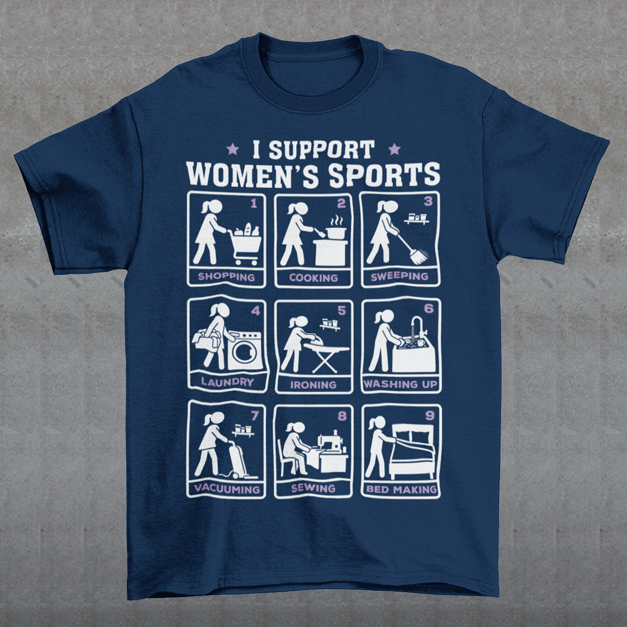 Navy t-shirt featuring the humorous phrase “I SUPPORT WOMEN’S SPORTS” with nine illustrated panels parodying different household activities: shopping, cooking, sweeping, laundry, ironing, washing up, vacuuming, sewing, and bed making. White and purple graphics create a retro sports-style design with a sarcastic, tongue-in-cheek theme.