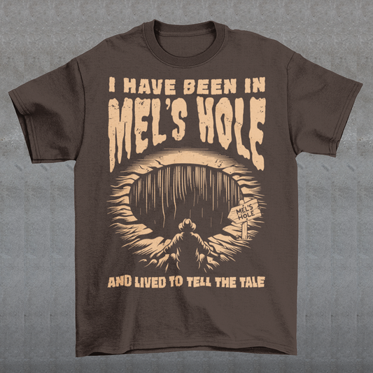 Step into the strange with this quirky and mysterious tee! Featuring a bold illustration of a curious man peering into a dark, bottomless abyss, this shirt pays homage to the legendary paranormal tale of Mel's Hole — a supposed infinite pit in the wilds of Washington State. The vintage-style artwork is topped with the eerie invitation: "VISIT MEL'S HOLE" in retro tourism font, blending humor, folklore, and a dash of the unexplained.