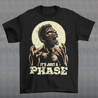 This t-shirt features a dynamic illustration of a man mid-transformation into a fearsome werewolf under the glow of a full moon. His human features contort as claws emerge, fur spreads across his body, and his eyes glow with a supernatural intensity. Below the image, the humorous and clever text reads: "IT'S JUST A PHASE," playfully alluding to both the lunar cycle and the werewolf's transformation.