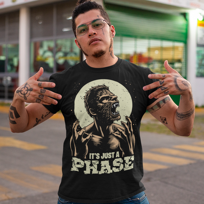 This t-shirt features a dynamic illustration of a man mid-transformation into a fearsome werewolf under the glow of a full moon. His human features contort as claws emerge, fur spreads across his body, and his eyes glow with a supernatural intensity. Below the image, the humorous and clever text reads: "IT'S JUST A PHASE," playfully alluding to both the lunar cycle and the werewolf's transformation.