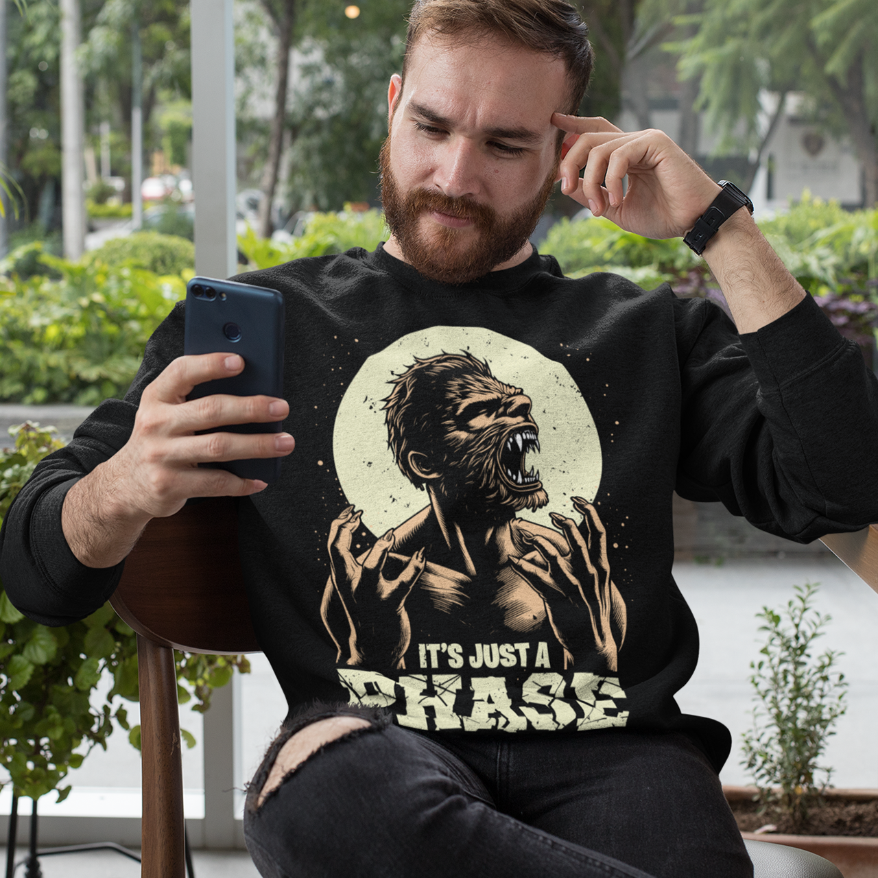 Black sweatshirt of a man transforming in to a werewolf with text underneath "IT'S JUST A PHASE."