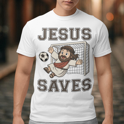 White t-shirt featuring a cartoon of Jesus as a soccer goalie diving to block a ball in front of a goal net, with the bold text “Jesus Saves” above and below. Fun, humorous Christian design combining faith and sports, printed on a clean white background.