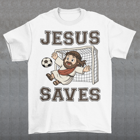 White t-shirt featuring a cartoon of Jesus as a soccer goalie diving to block a ball in front of a goal net, with the bold text “Jesus Saves” above and below. Fun, humorous Christian design combining faith and sports, printed on a clean white background.