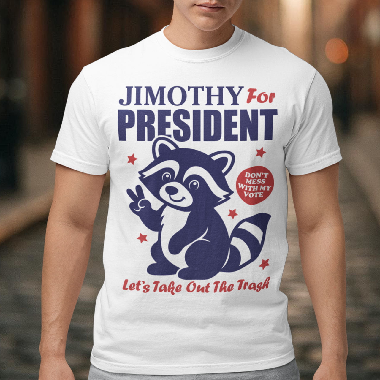 White t-shirt featuring a funny Jimothy the raccoon meme design with the text “JIMOTHY FOR PRESIDENT” in bold blue and red lettering. A cartoon raccoon gives a peace sign alongside the slogan “DON’T MESS WITH MY VOTE” and “LET’S TAKE OUT THE TRASH,” with red stars surrounding the patriotic graphic. Perfect for raccoon lovers, meme fans, and political humor enthusiasts.