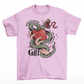 Pink t-shirt of a hand holding an apple wrapped in a snake with text around "KNOWLEDGE IS THE GREATEST GIFT".