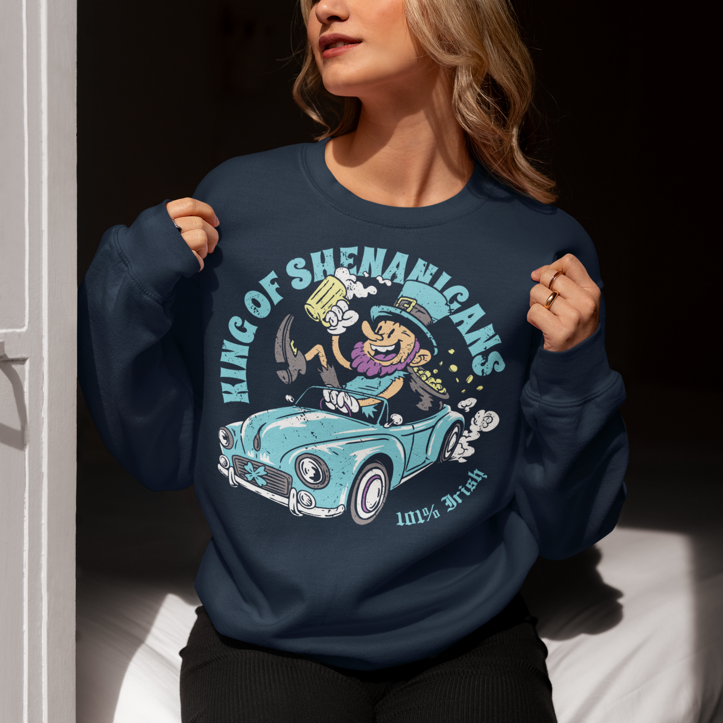 Navy sweatshirt with a leprechaun driving a car with text KING OF SHENANIGANS.