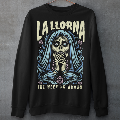 This striking La Llorona sweatshirt features a haunting depiction of the legendary Weeping Woman, her ghostly figure shrouded in mist, with flowing hair and a sorrowful expression as she searches for her lost children. The design captures the eerie, chilling essence of the famous Latin American folktale, blending dark, gothic tones with an ethereal glow. Above the image, bold lettering reads "LA LLORONA", while below, the translation "THE WEEPING WOMAN" adds to the eerie mystique.