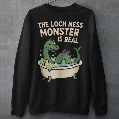 This black graphic sweatshirt puts a playful spin on legendary folklore with an adorable take on the Loch Ness Monster. Featuring a cheerful green Nessie splashing in a clawfoot bathtub with bubbles and a rubber duck, the design pairs cozy humor with cryptid charm. Bold lettering declares “The Loch Ness Monster Is Real,” delivering the punchline with confidence and a wink.