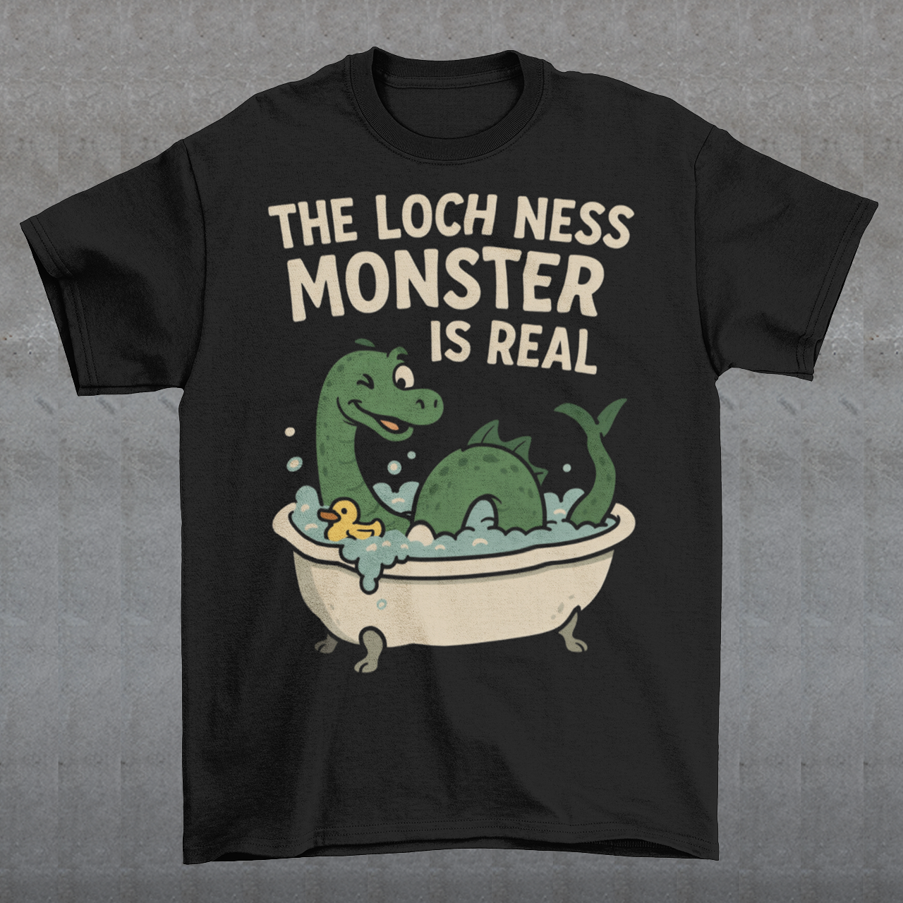 This black graphic tee puts a playful spin on legendary folklore with an adorable take on the Loch Ness Monster. Featuring a cheerful green Nessie splashing in a clawfoot bathtub with bubbles and a rubber duck, the design pairs cozy humor with cryptid charm. Bold lettering declares “The Loch Ness Monster Is Real,” delivering the punchline with confidence and a wink.