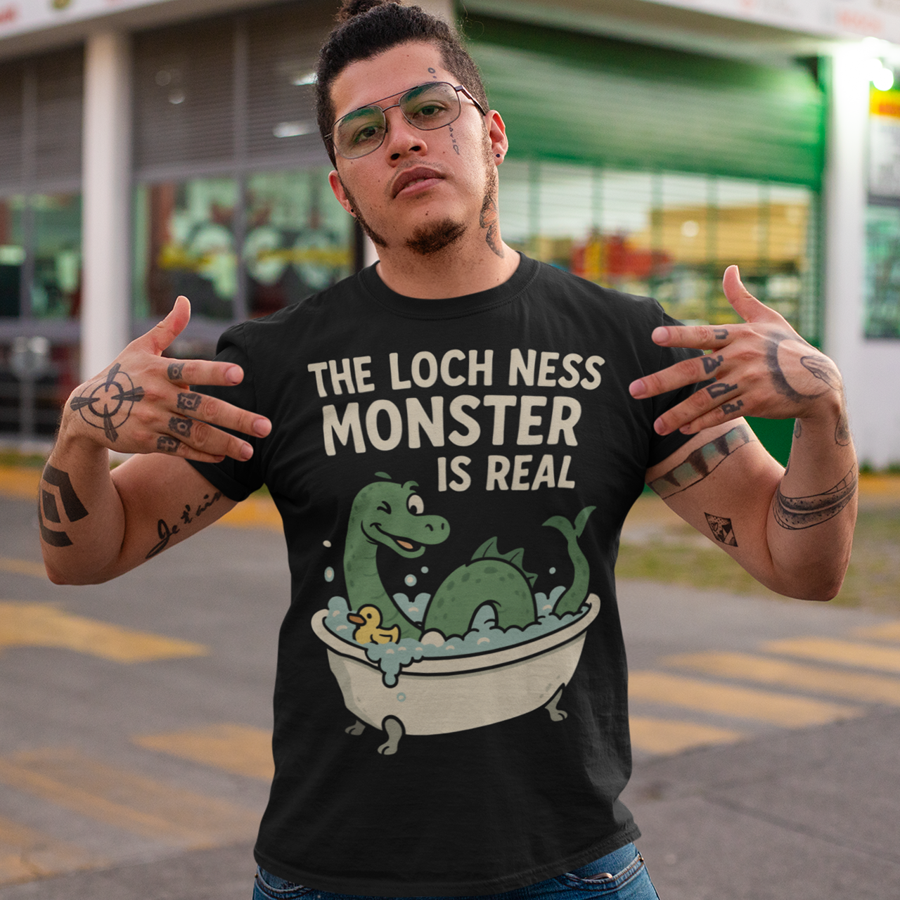 This black graphic tee puts a playful spin on legendary folklore with an adorable take on the Loch Ness Monster. Featuring a cheerful green Nessie splashing in a clawfoot bathtub with bubbles and a rubber duck, the design pairs cozy humor with cryptid charm. Bold lettering declares “The Loch Ness Monster Is Real,” delivering the punchline with confidence and a wink.