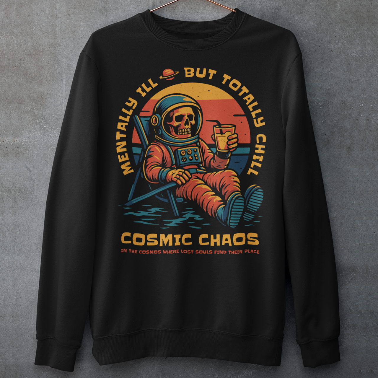 This black graphic sweatshirt features a laid-back skeleton astronaut floating in cosmic calm, drink in hand, as the universe quietly burns behind him. Bold retro colors and sunset tones frame the scene, while the phrase “Mentally Ill But Totally Chill” wraps the design with dark humor and self-aware wit. Anchored by the tagline Cosmic Chaos, it feels like a space-age postcard from the edge of existence.